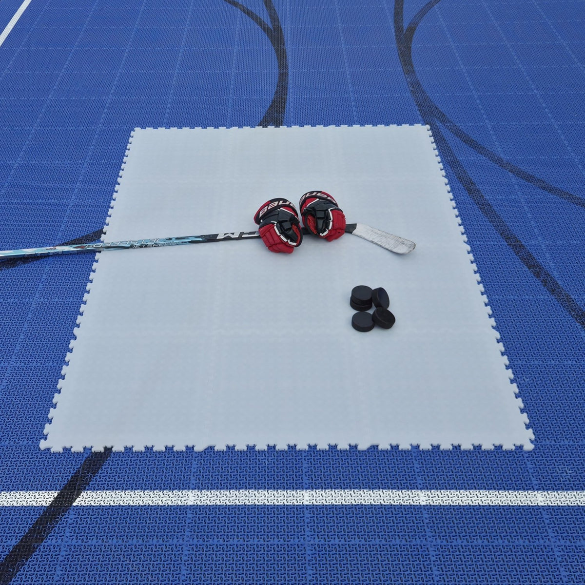 Everyday Ice white interlocking dryland hockey training surface set up on a blue sports floor with stick, gloves, and pucks.
